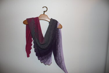 Gestrickter Drachenschwanz-Schal mit Farbverlauf (Magenta–Grau–Lavendel) an Holzkleiderbügel vor heller Wand.