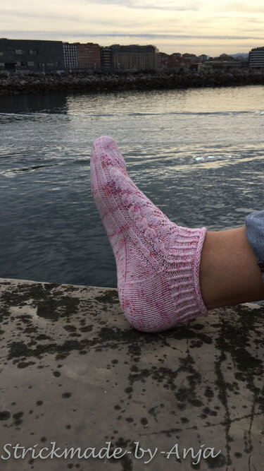 Fuß mit rosa-melierter handgestrickter Knöchelsocke vor Wasser
