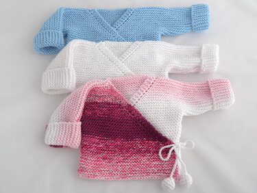Drei gestrickte Wickeljacken für Babys in Blau, Weiß und Rosa, kraus rechts gestrickt mit Umschlagbündchen und Bindeband