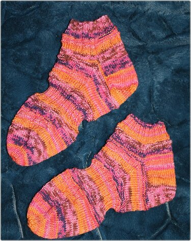 Paar handgestrickter knöchelhoher Socken in Orange, Pink und Violett auf dunklem Stoff