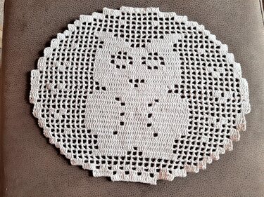 Weißes rundes Häkeldeckchen mit Eulenmotiv auf braunem Stoff