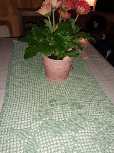 Hellgrüner gehäkelter Tischläufer mit rosa Blumentopf auf weißer Tischdecke