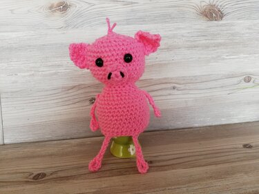 Rosa gehäkelter Schweinchen-Eierwärmer auf grünem Eierbecher vor hellem Holzuntergrund