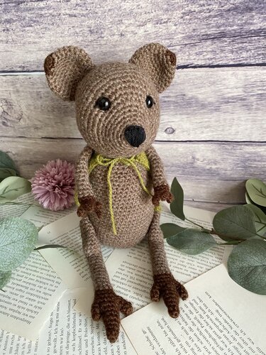 Braunes gehäkeltes Amigurumi-Häkeltier mit grüner Schleife auf aufgeschlagenem Buch