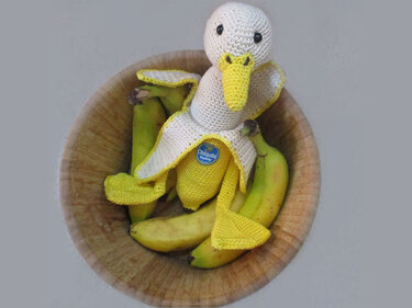 Handgehäkelte Ente in Bananenschale zwischen Bananen in einer Holzschale