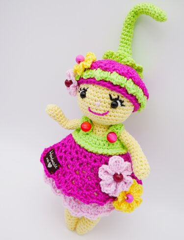 Handgehäkelte Amigurumi-Puppe mit spitzem Hut, pink-grünem Kleid und Blumenapplikationen.