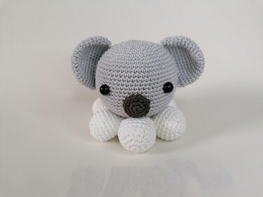 Gehäkelter Koala-Amigurumi, grau und weiß, mit schwarzen Augen auf hellem Hintergrund
