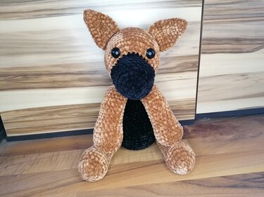 kuscheliger brauner Amigurumi-Hund mit schwarzem Maul vor Holzpaneelen