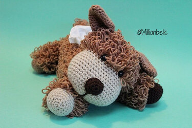 Brown curly crocheted puppy tissue box cover with beige muzzle on teal background
