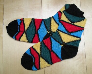 Paar gestrickter Damensocken mit diagonalen Rauten in Schwarz, Rot, Blau, Gelb und Grün auf hellem Holzuntergrund