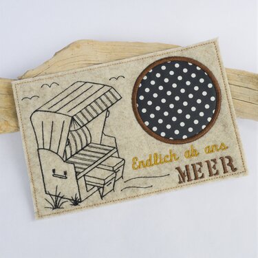 Heller Filz-Tassenteppich mit gesticktem Strandkorb, gepunkteter Kreisapplikation und dem Schriftzug „Endlich ab ans Meer“.