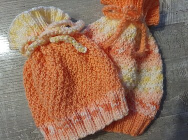 Nahaufnahme zweier gestrickter Babymützen in orange-pfirsich-Tönen mit Rippenbündchen, Strukturmasche und Bindekordel