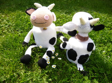 Zwei gehäkelte Kuhfiguren in Schwarz und Weiß auf grüner Wiese mit Gänseblümchen