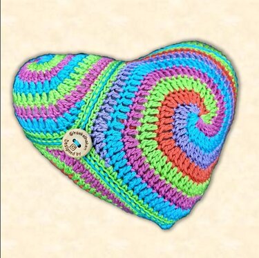 Heart-shaped crocheted pillow with multicolored spiral stripes and a wooden button
