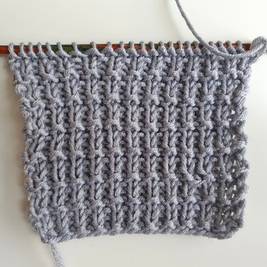 Grau texturiertes Strickmuster als Inspirationsprobe, teilweise auf Stricknadeln