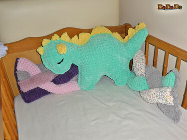 Gehäkeltes mintgrünes Dino-Kissen mit gelben Stacheln im Holz-Kinderbett