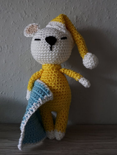 Crocheted yellow amigurumi bear wearing nightcap and holding a blue blanket