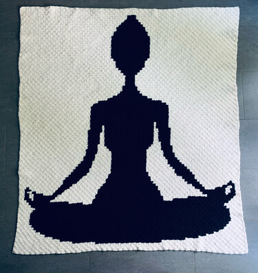 Gehäkelte weiße Decke mit schwarzer Silhouette einer meditierenden Person im Lotussitz.