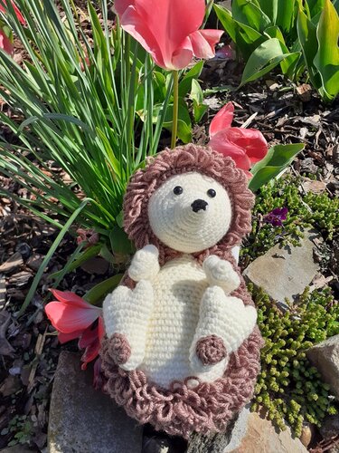 Gehäkelter Amigurumi-Igel auf dem Rücken zwischen Tulpen und Natursteinen