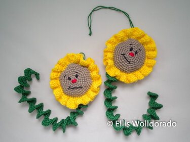 Zwei gehäkelte Sonnenblumen-Anhänger mit gelben Rüschenblüten und spiralförmigen grünen Stielen