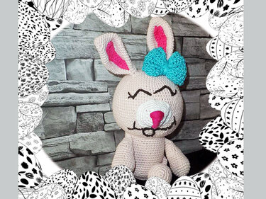 Gehäkelter beiger Amigurumi-Hase mit pinken Ohren und türkisfarbener Schleife, umrahmt von schwarz-weißen Ostereiern
