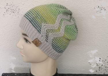 Gestrickte Beanie in Grün- und Grautönen mit Zickzack-Muster auf einem Schaufensterkopf