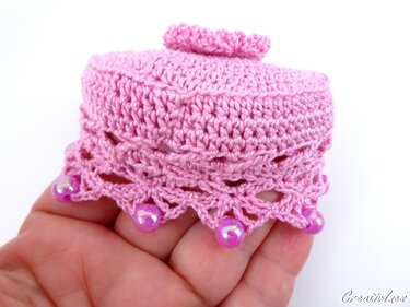 Kleine rosa gehäkelte Dose mit Spitzenrand und Perlen, gehalten in einer Hand