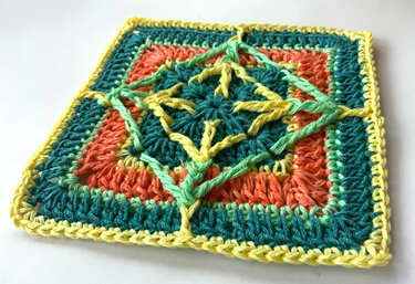 Gehäkeltes Quadrat mit reliefartigem Stern‑Kreuz‑Muster in Türkis, Koralle, Hellgrün und Gelb.