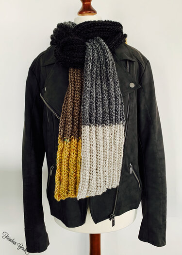 Grob gestrickter Rippenschal mit fünf klar getrennten Farbblöcken in Schwarz, Grau, Hellbeige, Braun und Gelb an einer Schaufensterpuppe.