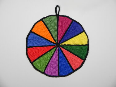 Gestrickter runder Topflappen mit farbigen Keilen, schwarzen Trennlinien und Aufhängeschlaufe