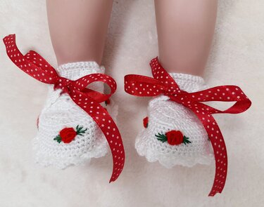 Weiße gehäkelte Babyschuhe mit rot gepunktetem Schleifenband und kleinem Rosenmotiv
