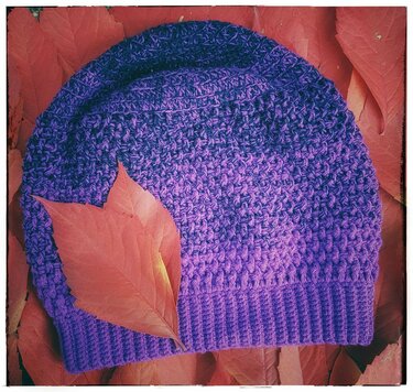 Violette gehäkelte Beanie mit Rippenbund auf roten Herbstblättern