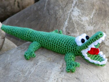 Grünes Amigurumi-Krokodil auf Stein, Maul geöffnet und Zähne sichtbar