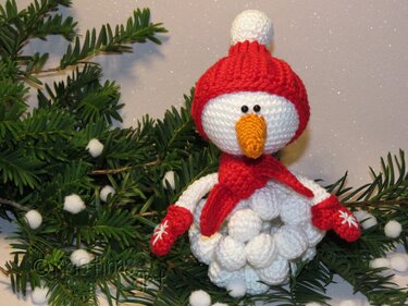 Gehäkelter Schneemann mit roter Mütze, Schal und Handschuhen auf Tannengrün