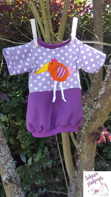 Lila Kinderkleid mit weißen Punkten, orangefarbener Vogel-Applikation und gerafftem Saum an einem Ast aufgehängt