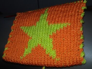 Gestricktes Quadrat mit leuchtend grünem Stern auf orangefarbenem Grund