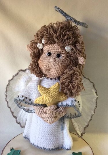 Nahaufnahme eines gehäkelten Amigurumi-Engels mit braunen Locken, weißem Kleid, Flügeln, Heiligenschein und gelbem Stern