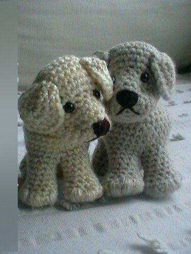 Zwei gehäkelte Amigurumi-Welpen, ein beiger und ein grauer Hund nebeneinander