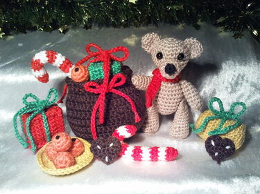 Gehäkelter Teddybär mit kleinen Geschenkpaketen, Zuckerstangen und Schokoladenherzen auf silbernem Stoff