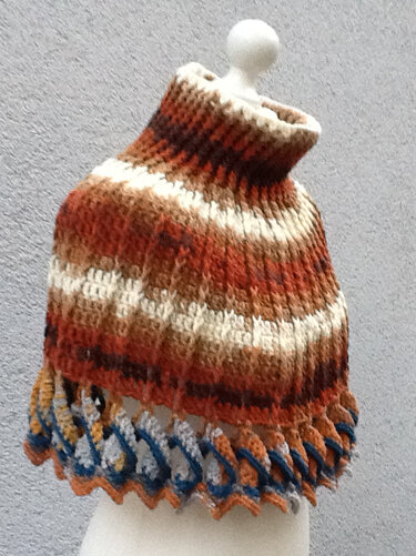 Gehäkelter Kragenschal in Braun-, Orange- und Cremetönen mit blauer und grauer Muschelkante auf einer Schaufensterpuppe.