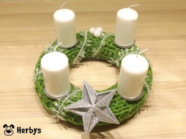 Gestrickter grüner Adventskranz mit vier weißen Kerzen und silbernem Stern auf hellem Holztisch