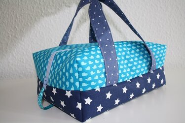 Kastenförmige Stofftasche türkis mit Walmotiv, dunkelblau mit weißen Sternen, gepunktete Tragegriffe und hellblauer Reißverschluss.