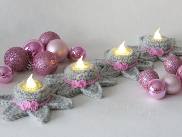 Gehäkelte graue Stern-Teelichthüllen mit rosa Zierband und LED-Lichtern, umgeben von rosa Christbaumkugeln