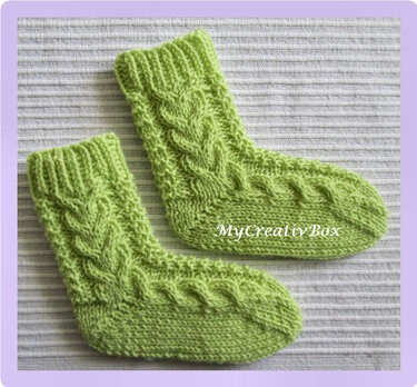 Hellgrüne gestrickte Kindersocken mit Zopfmuster auf hellem, geripptem Stoff