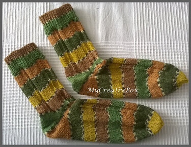 Paar gestrickter Socken mit breiten Streifen in Grün, Gelb und Braun auf hellem Untergrund.