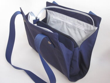 Dunkelblaue Stofftasche, offen, mit hellgrauem Innenfutter, mehreren Reißverschlüssen, Henkeln und verstellbarem Schultergurt.