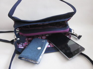 Geöffnete dunkelblaue Umhängetasche mit gemustertem Innenfutter, Smartphone und Etui