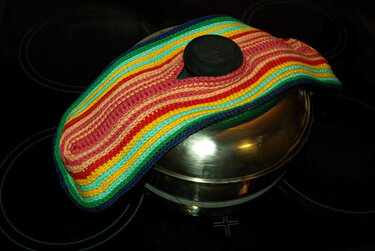 Gehäkelter Topfschoner in Regenbogenstreifen auf einem Metalltopf