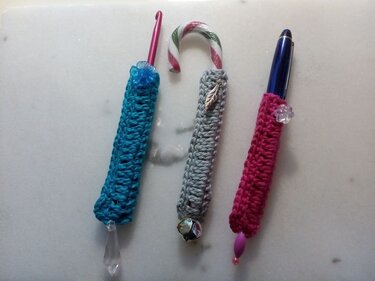 Drei schlanke gehäkelte Röhren als Hüllen für Stifte, Häkelnadel und Zuckerstange mit Perlen, Blatt und Kugel