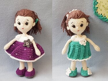Zwei gehäkelte Amigurumi-Puppen mit braunen Haaren, eine im lila Kleid mit Blume, eine im grünen Kleid mit weißer Blüte